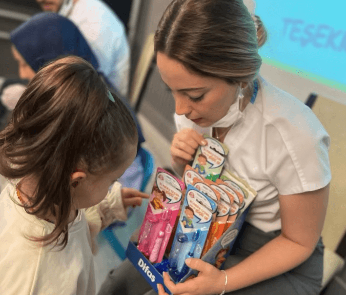 Bir eğitim etkinliği sırasında genç bir kıza çeşitli diş fırçalarını gösteren bir diş profesyoneli