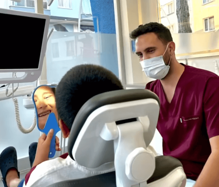 Bir diş hekiminin bir çocuk hastayı diş kliniğinde muayene ederken gülümsemesi